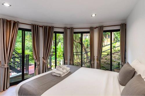 a bedroom with a white bed and large windows at Zen MaeKampong Waterfall Villa in Ban Huai Kaeo