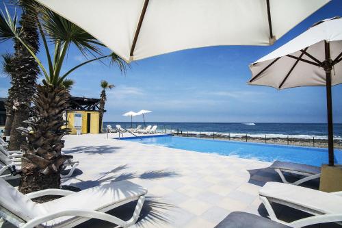 una piscina con sillas, una sombrilla y el océano en Panamericana Hotel Arica, en Arica
