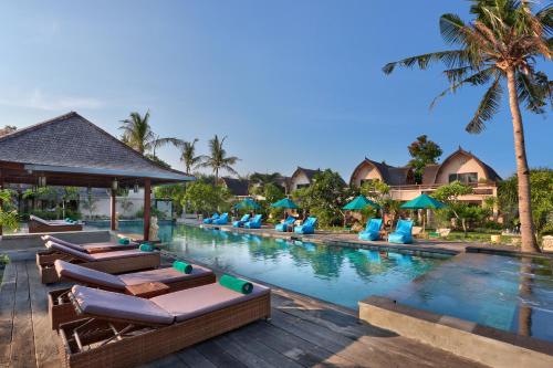 a pool at a resort with lounge chairs and palm trees at Vila Ombak in Gili Trawangan