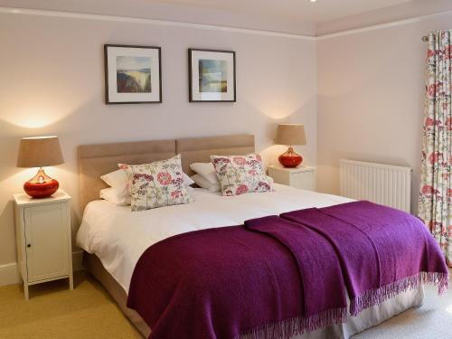a bedroom with a large bed with purple sheets and pillows at Prideaux Farmhouse in Luxulyan