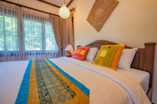 a bedroom with a large bed with colorful pillows at มนต์เมืองเชียงใหม่ รีสอร์ต Monmuang Chiangmai Resort in Hang Dong