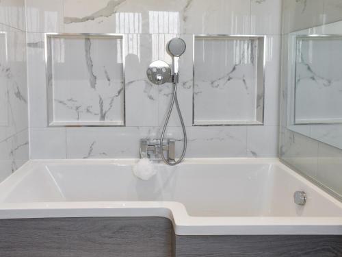 a white bath tub with a shower and two windows at The Hawthorns in Seaham