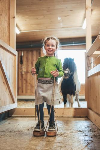 a little girl holding two ropes in a barn with a cow at Almfamilyhotel Scherer in Obertilliach