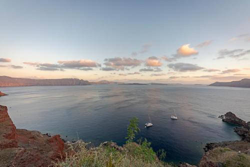 two boats in a large body of water at sunset at Helianthus Dream Homes in Oia