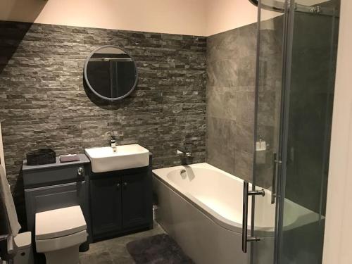 La salle de bains est pourvue d'un lavabo, d'une baignoire et d'un miroir. dans l'établissement Modern 3 Bed Barn Conversion in Great Urswick, à Great Urswick
