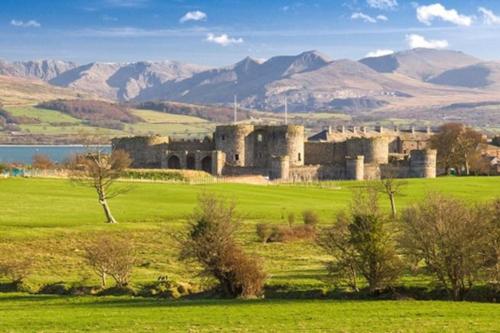 an old castle in a field with mountains in the background at Perfect 4 Cpls & Families . Close to Everything in Pentraeth