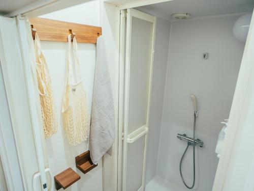 ein Bad mit einer Dusche und Handtüchern, die an einer Tür hängen in der Unterkunft ゲストハウスVACILANDO in Chitose