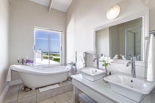a white bathroom with a tub and a sink and a mirror at 138 Marine Beachfront Guesthouse in Hermanus