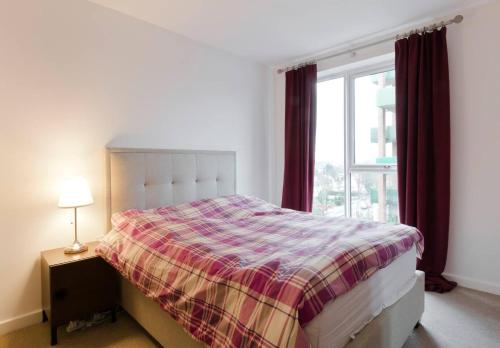 1 dormitorio con 1 cama con manta a cuadros y ventana en 2-Bed Apartment only 15 mins from Central London, en Londres