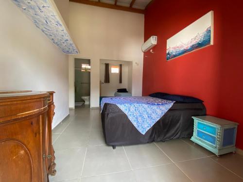 1 dormitorio con cama y pared roja en Casa em condomínio a 500m da praia de Pernambuco ideal para família, en Guarujá