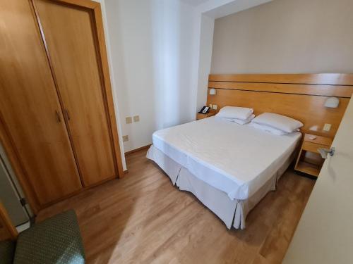 um quarto com uma cama branca e uma cabeceira em madeira em Wafeh Flats em San Diego Lourdes em Belo Horizonte