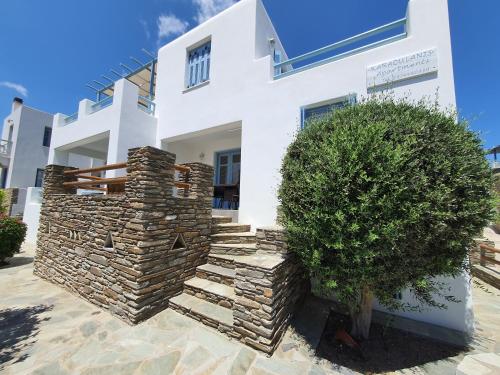 a white house with a stone wall and a tree at Karaoulanis Apartments in Andros