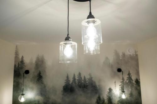 three lights hanging from a ceiling with a forest painting at The Francis Boutique Inn in Ucluelet