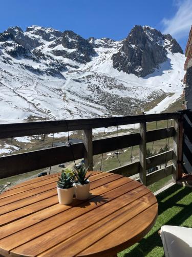 a wooden table with two plants on a balcony with a snow covered mountain at Chaleureux T2 au pied des pistes. Appt de 4 à 6 personnes. in La Mongie