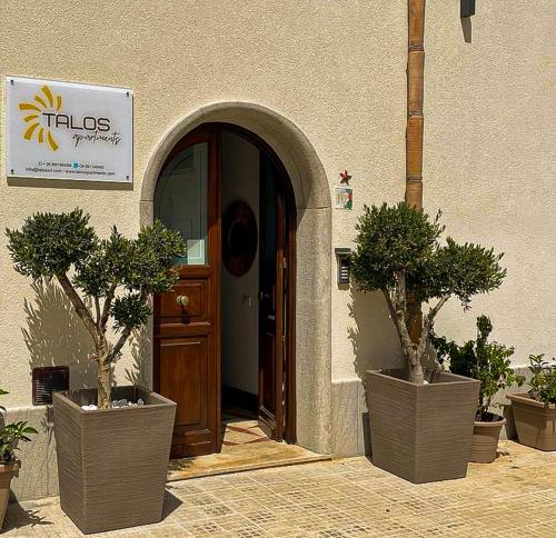 une porte menant à un bâtiment avec deux arbres en pot devant lui dans l'établissement Talos Apartments, à San Vito Lo Capo