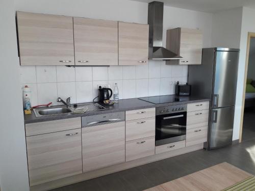 a kitchen with wooden cabinets and a stainless steel refrigerator at Fewo Steinhohle, DG 45qm, 1 Schlafzimmer & 1 Wohn-Esszimmer mit Bett in Sulzbach am Main