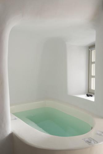 a bath tub in a white room with a window at Nisó Cave Suites in Megalokhori