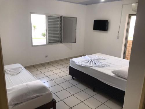 a bedroom with two beds and a television in it at Pousada dos Eletricitarios in Praia Grande