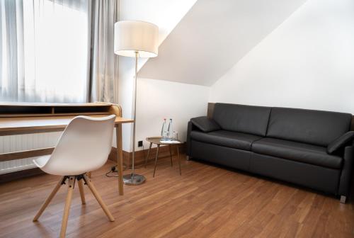 ein Wohnzimmer mit einem schwarzen Sofa und einem weißen Stuhl in der Unterkunft Stadthotel Heilbronn in Heilbronn