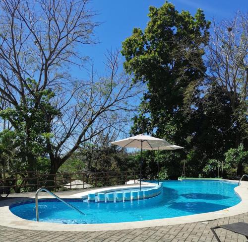 a large swimming pool with an umbrella and chairs at Casa de playa Herradura con piscina y jacuzzi in Puntarenas