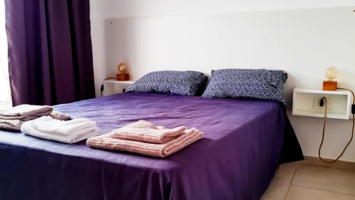 uma cama com lençóis roxos e toalhas em VB Home em Posadas