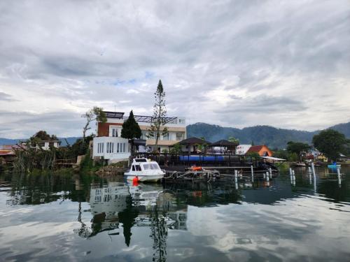 a small boat in a body of water with houses at PURNAMA BALIGE HOTEL in Balige
