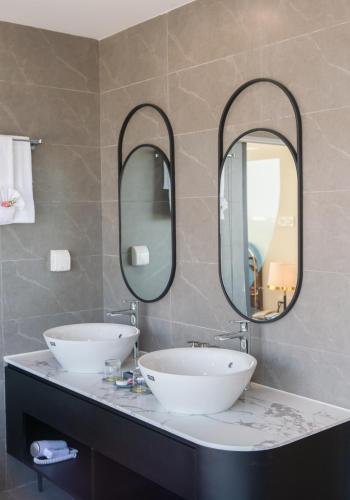a bathroom with two sinks and two mirrors at Grand Tourane Nha Trang Hotel in Nha Trang