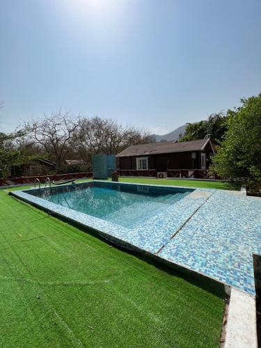 a large swimming pool with green grass and a house at Namanbagh in Alwar