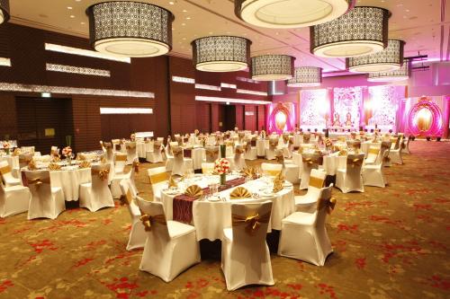 a banquet hall with white tables and chairs and chandeliers at Novotel Pune Viman Nagar Road in Pune