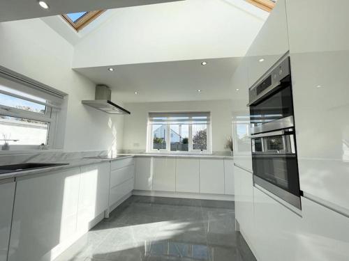 a large white kitchen with white cabinets and windows at Beautiful Bungalow near to Beach in Selsey