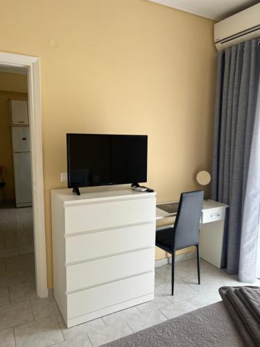 a television on a dresser with a desk and a chair at Comfort apartment for small family in Loutraki