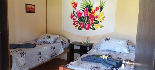 two beds in a room with a painting on the wall at Camping Hostal Tipanie Moana Aeropuerto Centro in Hanga Roa