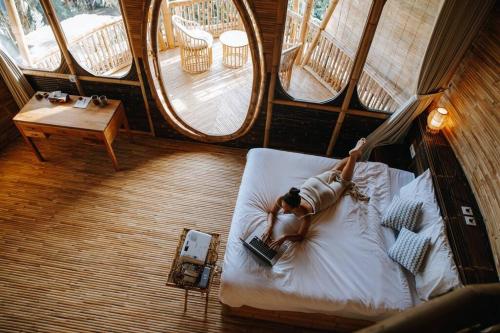 una donna sdraiata in un letto in una stanza con finestre di Tropical Bali Bamboo Villa - 7 Minutes from Canggu a Dalung