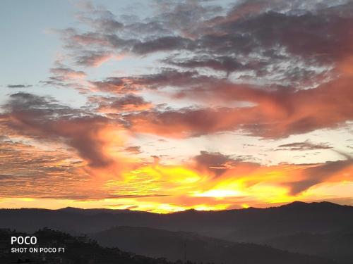 a sunset with clouds and mountains in the background at MangalMurti Himalyan Hotel in Almora