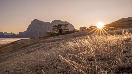 a house on a hill with the sun in the sky at Hotel Goldknopf in Alpe di Siusi