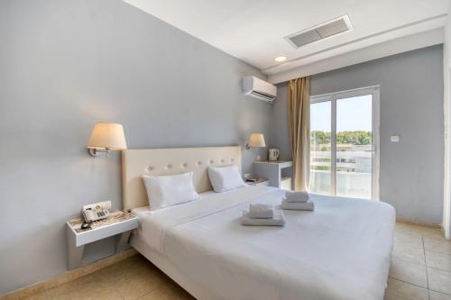 - une chambre blanche avec un grand lit blanc et une fenêtre dans l'établissement Astron Hotel Rhodes, à Rhodes