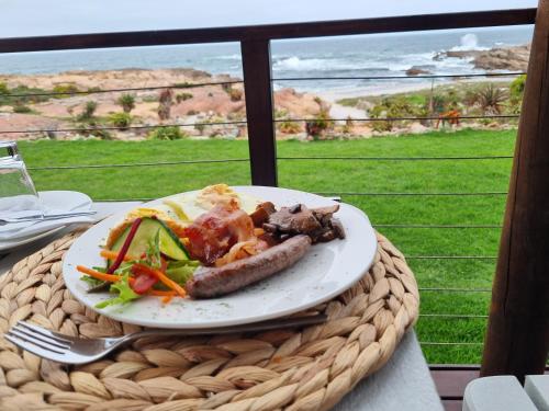 a plate of food on a table with a view of the ocean at Lambertsbay Beachfront in Lambertʼs Bay