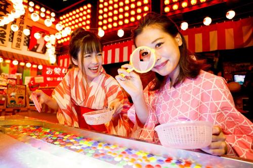 dos mujeres de pie detrás de un mostrador jugando un juego en Ooedo Onsen Monogatari Minoh Kanko Hotel, en Minō