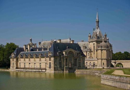 ein großes Schloss auf einem Wasserkörper in der Unterkunft L’escale proche château de chantilly in Précy-sur-Oise