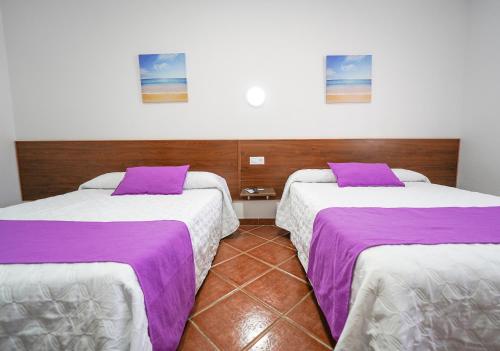 two beds in a room with purple and white sheets at Hostal Los Mellizos in Conil de la Frontera