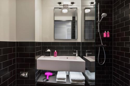 ein Badezimmer mit einem weißen Waschbecken und einem Spiegel in der Unterkunft Moxy Frankfurt Airport Kelsterbach in Kelsterbach