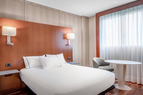 ウエルバにあるAC Hotel Huelva by Marriottの白い大型ベッドとテーブルが備わるホテルルームです。