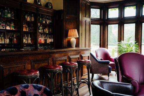 a bar with red stools in a room with windows at The Manor House Hotel and Golf Club in Castle Combe