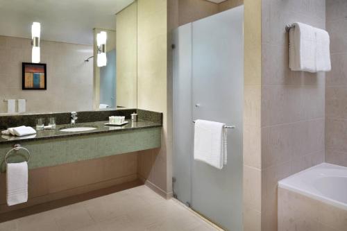 a bathroom with a sink and a mirror and a tub at Courtyard By Marriott Kuwait City in Kuwait