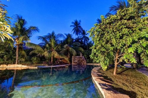a swimming pool with palm trees in a resort at Ganesh Lodge in Candidasa