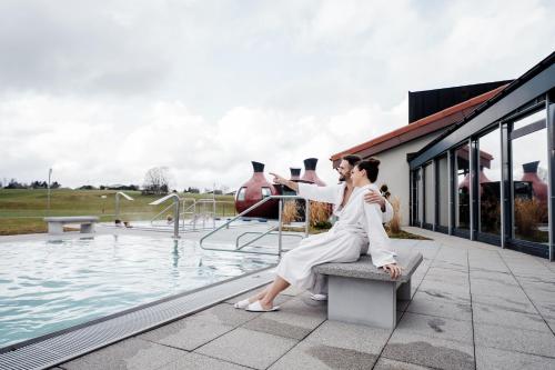 a woman sitting on a bench next to a swimming pool at Jura Sport & Spa Resort in Saignelégier