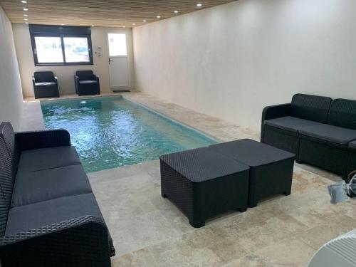 - une piscine avec des chaises, un canapé et une table dans l'établissement Villa piscine/spa privé intérieur 33° ZOO DE LA FLECHE 24h DU MANS, à La Flèche