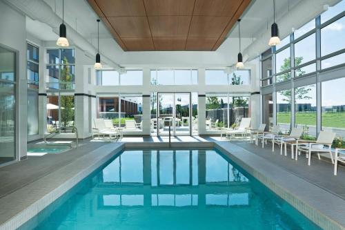 uma piscina interior com cadeiras brancas e janelas em Element Vaughan Southwest em Vaughan