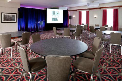 Four Points by Sheraton Hotel & Conference Centre Gatineau-Ottawa في غاتينو: قاعة اجتماعات مع طاولات وكراسي وشاشة
