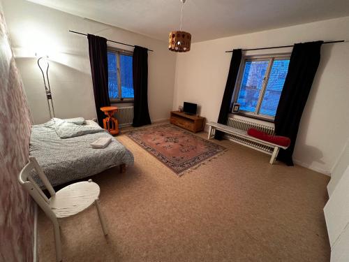 ein Schlafzimmer mit einem Bett und einem Stuhl sowie zwei Fenstern in der Unterkunft Ljungaverk Stor Lägenhet Med Öppen Spis in Ljungaverk